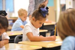 A student writes on her paper with a pencil