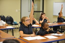 A couple students raising their hands in class to learn